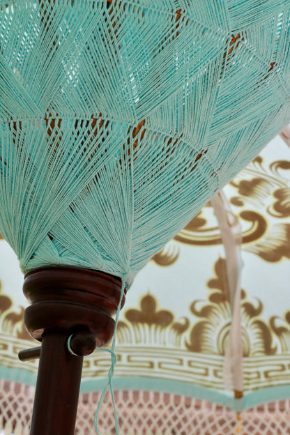Light blue Balinese-style garden parasol with white tassels and hand painted gold detail in an English garden