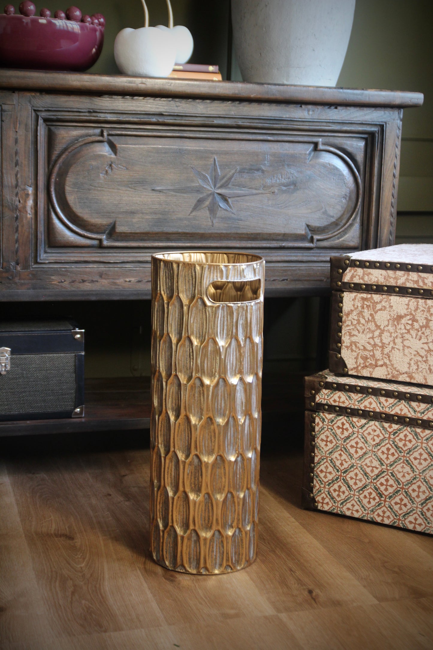 Gold umbrella stand with textured finish and cut-out handles shown in an interior.