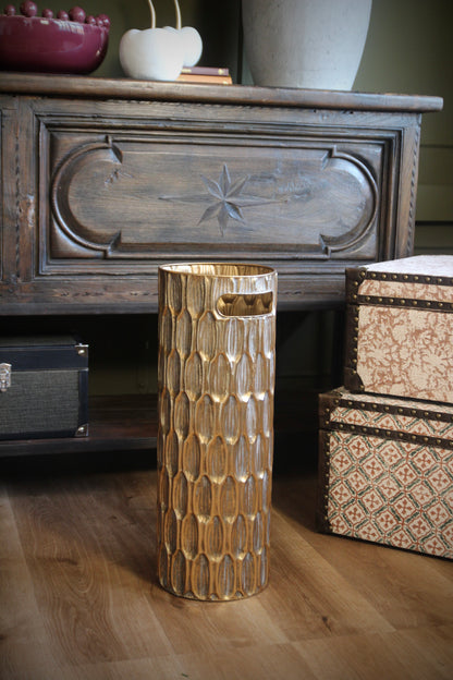 Gold umbrella stand with textured finish and cut-out handles shown in an interior.